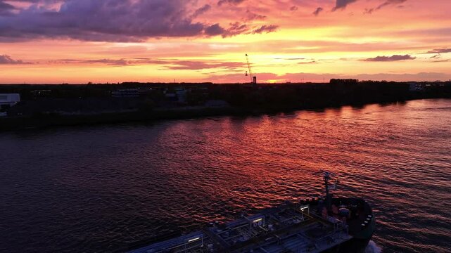 Colourful dramatic sky, land silhouettes, rippling water, container vessel