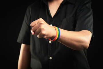 Hand fist with rainbow wristband in a hand while standing against a black background.