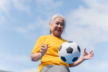 Active senior woman playing football in the urban outdoor court, Asian senior woman with a soccer...