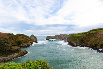 breathtaking landscape of green mountains and cliffs next to the green sea with blue sky and copy space. Bellerin beach Cantabria Spain.