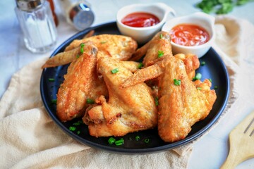 Fried chicken wing on a black plate with potato and chili sauce, home made