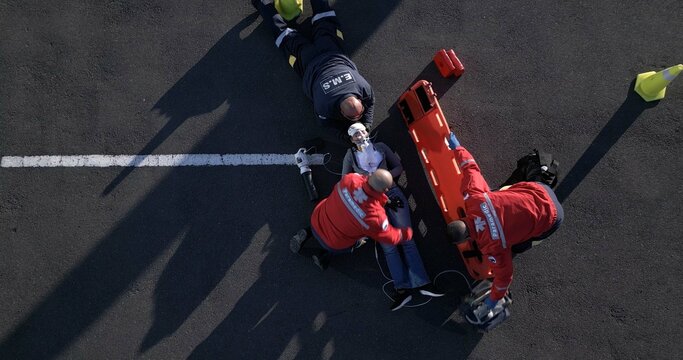 Accident, emergency and first aid with paramedic team on street from above for medical treatment. Healthcare, medicine and group of EMT people on road with patient for assessment, CPR or response