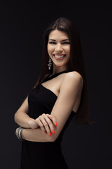 Naklejka premium An elegant young woman wearing a chic black dress stands with crossed arms against a dark background, exuding confidence and style.