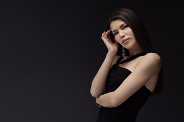 A graceful woman in a sophisticated black evening dress, showcasing elegance and a touch of mystery in her stance, isolated on a dark backdrop, creating a luxurious and elite feel.