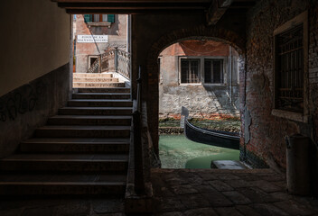 Gondola entering stone opening to canal near bridge in Venice, Italy.