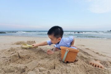 Asian young boy playing sand and toy on beach in day with clear vibe