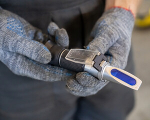 Fototapeta premium A mechanic holds a Refractometer in a car service center. Portable optical device for determining the freezing point of antifreeze.