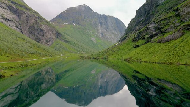 A serene video of a lake encircled by tall mountains. Tranquil scene with mountain and grass reflections in clear water. Norweigan Fjords Stavbergvatnet Urke