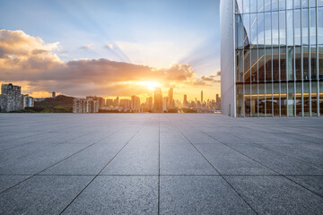 Empty square floor and glass wall with modern city buildings scenery at sunrise