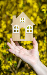 The girl holds the house symbol against the background of blossoming forsythia