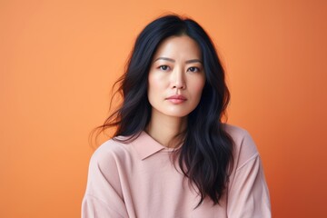 Obraz premium Portrait of a sad woman, 41, Asian, feeling homesick, on a pastel peach background