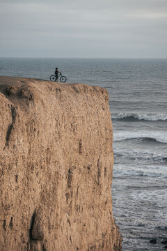 Woman mountain biker enjoying the sunset from the cliff next to ocean