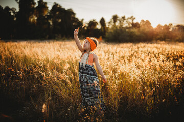 Young Girl in orange boho dress standing in field with golden light