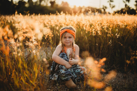 Young Girl in orange boho dress standing in field with golden light