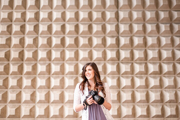 Happy women in front of unique wall holding camera looking off t