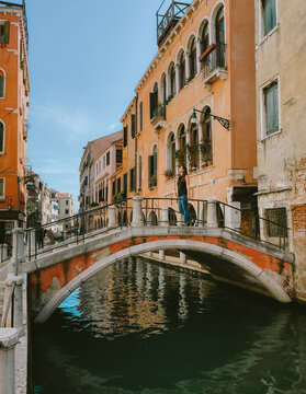 Woman standing on bridge crossing canal in Venice, Italy.