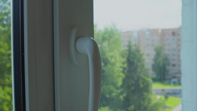 A hand closes the window sash. Close-up.