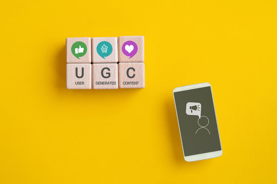 User-generated content concept. UGC, Online marketing concept. Customer create content on social media . Top view of  wooden cube with UGC icons and abbreviation with mobile phone on yellow background