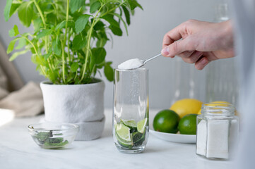 Homemade mojito making process, pouring sugar in glass with mint and lime, preparing summer fresh cocktail drink, lifestyle kitchen interior