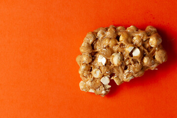 On an orange background, a piece of Chickpea (chana dal) chikki. Top-down view. Food Flat lay.