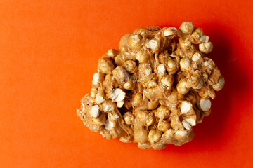 On an orange background, a piece of Chickpea (chana dal) chikki. Top-down view. Food Flat lay.
