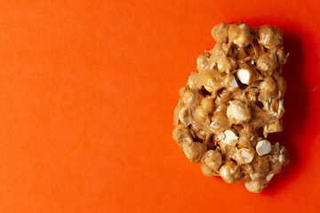 On an orange background, a piece of Chickpea (chana dal) chikki. Top-down view. Food Flat lay.
