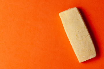 On an orange background, one sweet and tasty coconut butter cookie. Top-down view. Food Flat lay.