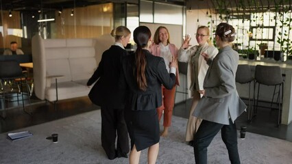 A group of confident businesswomen in business suits dance on a gray carpet in a modern office after success in business