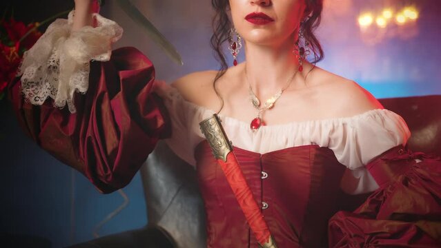 Close-up hands beauty woman hands hold weapon metal knife. Fantasy queen sitting on throne takes dagger out sheath, blade glistens in candle light. Evil vampire girl sexy red dress dark room art 4k