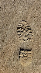 A prominent trainer shoeprint marked by a deep tread pattern is embedded in the sand.