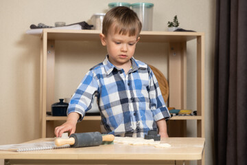 Little boy making cookies using cookie cutters and dough in the kitchen.