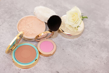 Bronzer, powder, blusher, brush and rose flower on grey textured table, above view