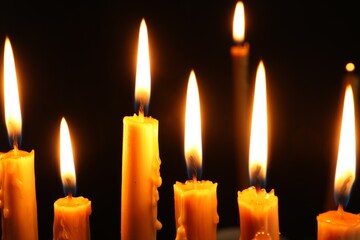 Many burning church candles on black background, closeup