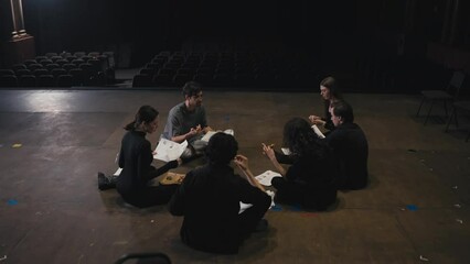 Happy group of actors holding script sheets in their hands and actively discussing their roles with the director on stage in the theater during rehearsal
