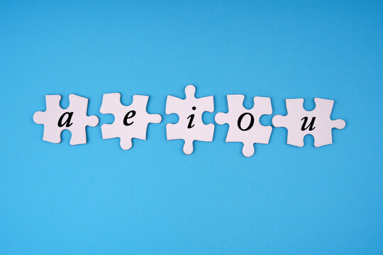 Communication, learning and education concept. The vowels aeiou written on jigsaw puzzle pieces. With light blue background.