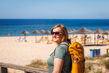 Middle aged female tourist admiring Praia de Alvor beach after hike in Algarve, Portugal. Woman is enjoying active summer vacation