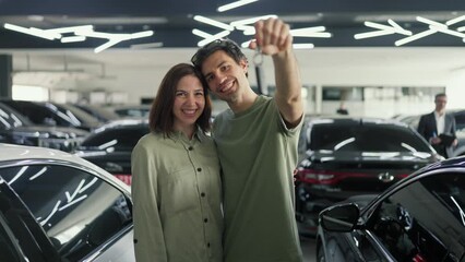 Portrait of a happy couple a brunette guy in a Green T-shirt brings the key to his new car up while his girlfriend hugs him happy couple got a new car in a car showroom