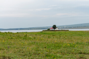 A small church with a red roof on a flowering field surrounded by a stone fence. Lake, mountains