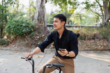 Young Man Riding Bicycle and Using Smartphone Outdoors, Eco-Friendly Lifestyle Concept of...