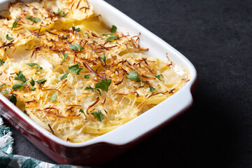 Potato gratin baked with cream and cheese on black slate background. Copy space