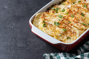 Potato gratin baked with cream and cheese on black slate background. Copy space