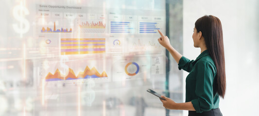 Professional woman interacting with digital sales dashboard displaying various charts and graphs in modern office.