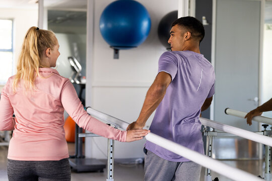 A biracial man and female physical therapist use parallel bars for rehabilitation