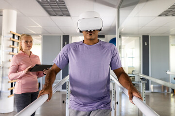 A biracial man wearing VR headset using parallel bars for rehabilitation