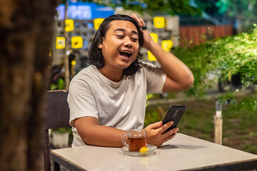 Young Asian man, digital nomad working remotely from cafe, using laptop and smartphone. young Asian men are hanging out in a cafe with a nature theme at night