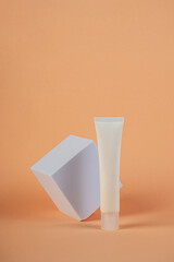 Plastic white tube for cream or lotion. Skin care or sunscreen cosmetic with stylish props on cream background.