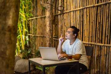 Young Asian man, digital nomad working remotely from cafe, using laptop and smartphone. young Asian men are hanging out in a cafe with a nature theme at night