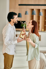 A beautiful adult couple, a redhead woman and bearded man, exchanging gifts in a modern apartment living room.