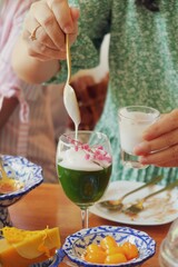 Image of a traditional green drink with coconut cream and pink flowers being prepared, accompanied by colorful desserts on a festive table. Perfect for a casual gathering or celebration.
