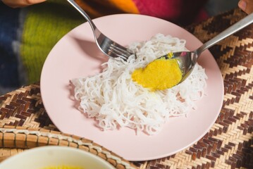 Close-up of a khanom jeen, traditional dish with noodles and yellow curry on a pink plate, captured on a woven mat. Perfect for illustrating Southeast Asian or Indian cuisine and cozy dining settings.
